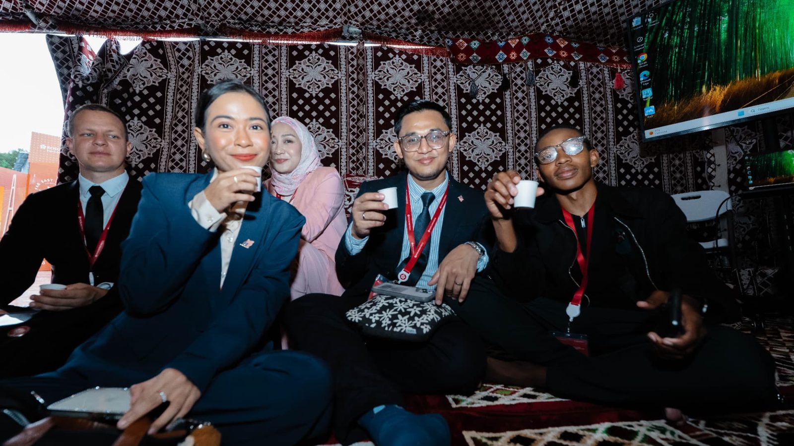 A group of forum delegates sitting together on patterned carpets, each holding a small cup.